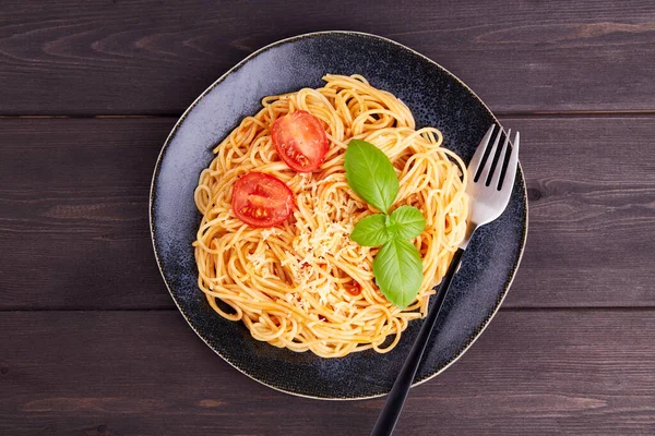 Domatesli spagetti, domates sosu, fesleğen ve siyah tabakta parmesan. Geleneksel İtalyan pastası. Üst görünüm, kopyalama alanı, yakın plan..