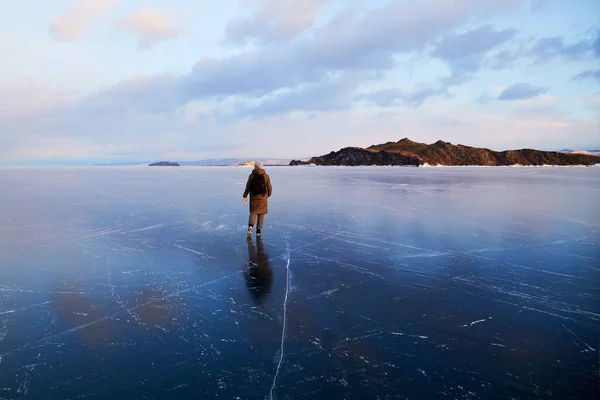 Una joven viaja en invierno. Hielo transparente de un lago congelado al atardecer. —  Fotos de Stock