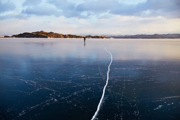 Un hombre camina sobre el hielo del lago Baikal. Una gran grieta en el hielo transparente del lago. —  Fotos de Stock