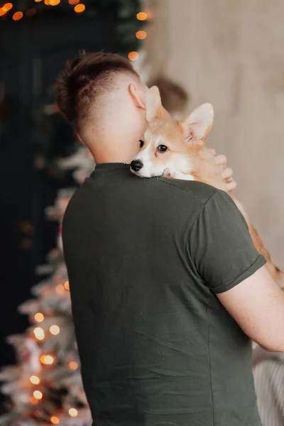 Genç adam kucağında küçük bir köpek tutuyor.