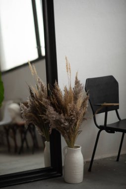 Evin dekorasyonunda aynanın yanındaki vazoda pofuduk kurumuş çiçekler.