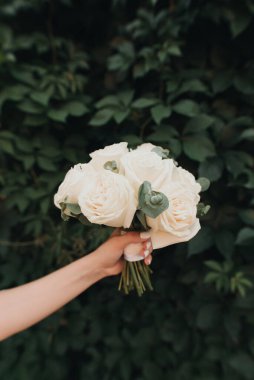 Yeşil yapraklardan oluşan arka planda küçük, temiz bir gelin buketi.