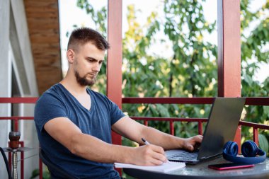 Sakallı genç bir adam dışarıda çalışmak için bilgisayar dizüstü bilgisayar kullanıyor, evde online olarak serbest çalışıyor, yakışıklı bir öğrenci okuyor, öğreniyor, çevrimiçi eğitim alıyor, serbest çalışıyor.