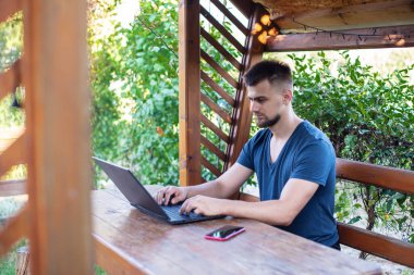 Sakallı genç bir adam dışarıda çalışmak için bilgisayar dizüstü bilgisayar kullanıyor, evde online olarak serbest çalışıyor, yakışıklı bir öğrenci okuyor, öğreniyor, çevrimiçi eğitim alıyor, serbest çalışıyor.