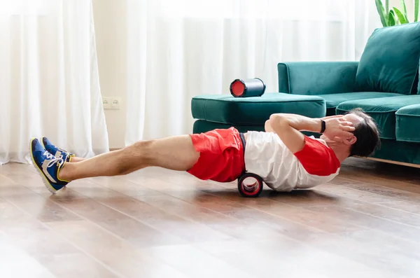 一位穿着红色短裤的年轻人正在泡沫滚筒上做运动 用按摩滚筒锻炼肌肉 运动员运动后用泡沫滚筒来减轻肌肉酸痛 — 图库照片