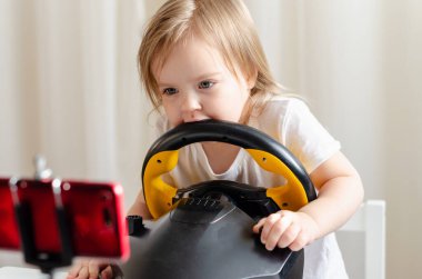 Küçük kız bilgisayar direksiyonuyla oynuyor. Video oyunu oynayan küçük bir kız. Araba yarışı. Geleceğin şoförü. Profesyonel sürüş için hazırlanıyorum. Araba süren çocuk.