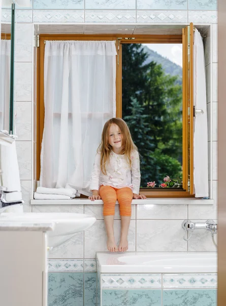 Cute little girl sitting on a bathroom window — Stock Photo, Image