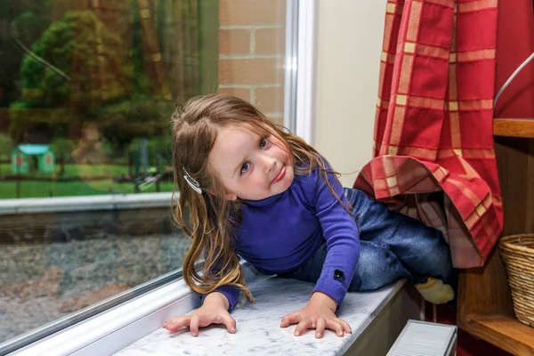 Niedliches kleines Mädchen, das mit Vorhängen am Fenster spielt — Stockfoto