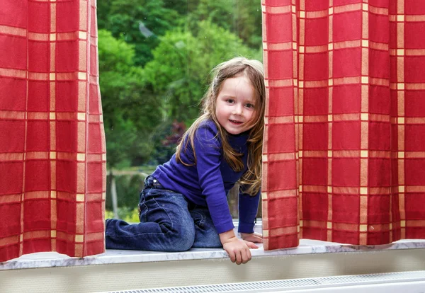 Niedliches kleines Mädchen, das mit Vorhängen am Fenster spielt — Stockfoto