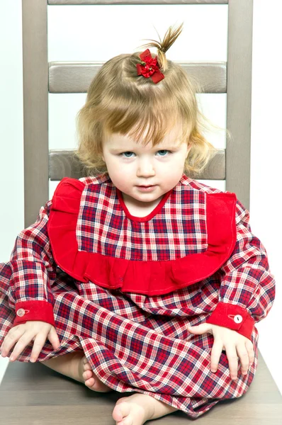 Schattig klein meisje in een rode jurk zittend op een stoel — Stockfoto