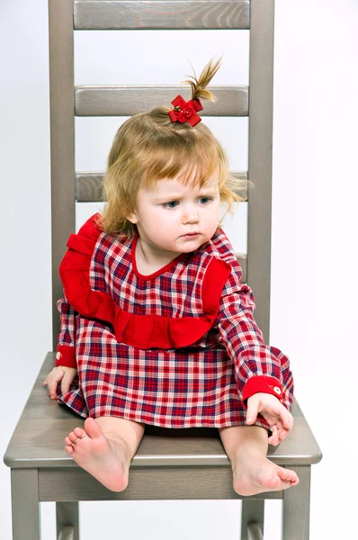 Söt liten flicka i röd klänning sitter på en stol — Stockfoto
