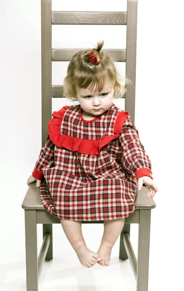 Schattig klein meisje in een rode jurk zittend op een stoel — Stockfoto