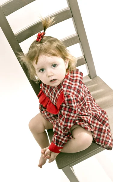 Menina bonito em vestido vermelho sentado em uma cadeira — Fotografia de Stock