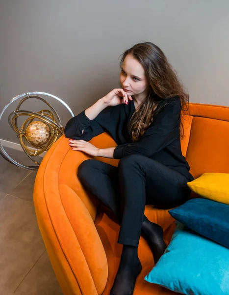 Güzel genç kız güzel turuncu bir kanepede poz veriyor..