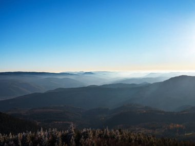 İlk kış soğuğu. Vosges dağlarının tepelerinde ağaçlar kırağı ile kaplıdır. Beyaz kar ve mavi gökyüzü. Dağların siluetlerinin panoramik görüntüsü.