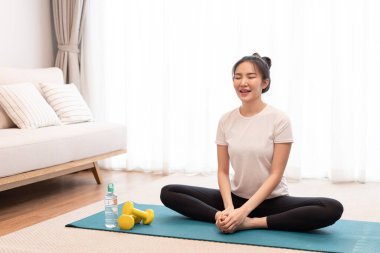 Topuzlu bir kız dikdörtgen yeşil bir mindere oturur ve bacaklarını yere paralel olarak uzatır..