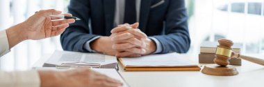 Hukuk konsepti. Koyu mavi takım elbiseli bir avukat masasında oturuyor ve beyaz gömlekli bir adam olan müşterisine hukuk danışmanlığı yapmaya hazırlanıyor..