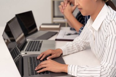 Beyaz çizgili tişörtlü kadın, iş arkadaşı siyah çizgili gömlekli adamla dizüstü bilgisayarların önünde çalışıyor..