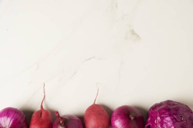 Sebze konsepti. Birkaç mor sebze, beyaz fayans masasında tek sıra halinde diziliyor..