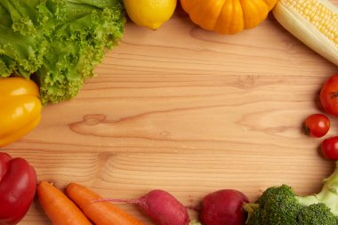 Sebze konsepti marul, limon, balkabağı, mısır, domates, brokoli, pancar kökü, dolma biber ve ahşap masaya konan havuç gibi çeşitli sebzeler.