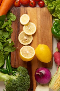 Sebze konsepti. Sarı limon dilimlerinin çoğu ahşap kesme tahtasına konur ve diğer sebzelerle çevrilidir..