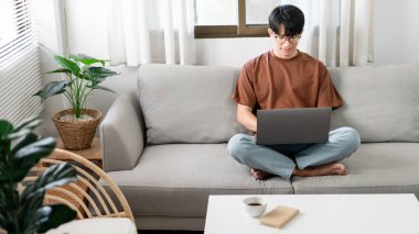 Teknoloji kavramı. Günlük giysiler giyen erkek kanepede oturuyor, dizüstü bilgisayarını dinlendiriyor ve işini yapıyor..