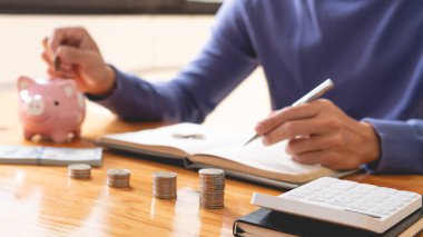 Tasarruf konsepti. Adam gelirini yazıyor ve biraz para biriktiriyor. Bu arada kumbaraya para atıyor..