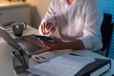 Fazla mesai. Masasında oturan ve bazı bilgileri aramak için akıllı telefonunu tutan ofis çalışanı hariç..