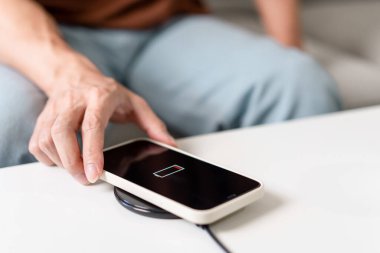 Teknoloji kavramı açık mavi kotuyla koltukta oturan ve akıllı telefonunu kablosuz pille şarj etmeye çalışan bir insan..