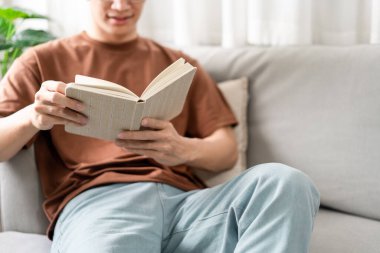 Teknoloji kavramı. Gözlüklü erkek gri koltukta oturuyor, sırtını yaslıyor ve kitap okuyor..