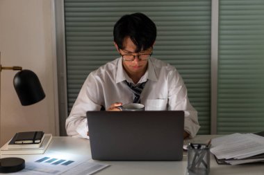 Fazla mesai. Geç saatlere kadar çalışıp, işine odaklanırken bir fincan kahve içen bir ofis çalışanı..