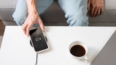 Teknoloji kavramı açık mavi kotuyla koltukta oturan ve akıllı telefonunu kablosuz pille şarj etmeye çalışan bir insan..