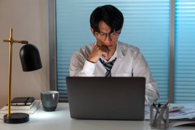 Aşırı çalışma kavramı. Gözlük takan erkek, çenesini sağ eline dayayıp sol elini kullanarak deftere harfler yazıyor..