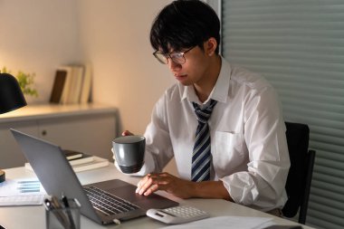 Fazla mesai. Geç saatlere kadar çalışıp, işine odaklanırken bir fincan kahve içen bir ofis çalışanı..