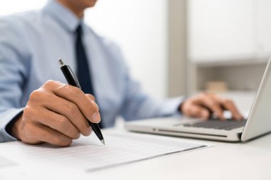 Çalışan Adam Conept ofiste oturan erkek subay sol elini dizüstü bilgisayara koydu ve sağ eliyle kağıda bir şeyler yazdı..