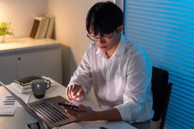 Fazla mesai. Masasında oturan ve bazı bilgileri aramak için akıllı telefonunu tutan ofis çalışanı hariç..