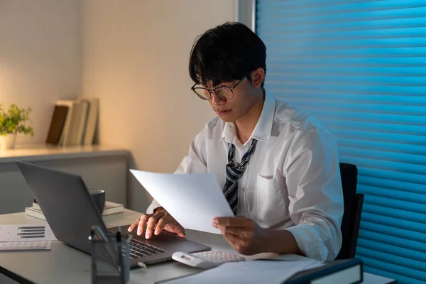 オーバーワークコンセプトデスクに座って書類を読み ノートを入力する緩いネクタイのオフィススタッフ — ストック写真