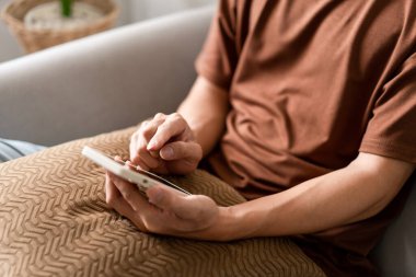 Teknoloji kavramı. Bir saksının yanında oturan adam kucağına küçük bir yastık koyuyor ve akıllı telefonundan bir şeyi kontrol ediyor..