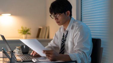 Fazla mesai. Ofis personeli masasında oturmuş, evrak okuyor ve not defterine yazı yazıyor..