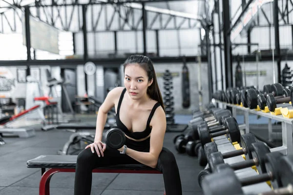 exercise concept The strong built woman in black sport top and pants and a smartwatch working out with the dumbbell by doing concentraction curl on her left arm.