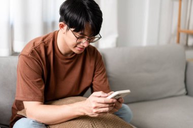 Teknoloji kavramı. Bir saksının yanında oturan adam kucağına küçük bir yastık koyuyor ve akıllı telefonundan bir şeyi kontrol ediyor..