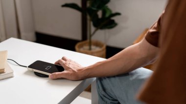 Teknoloji kavramı açık mavi kotuyla koltukta oturan ve akıllı telefonunu kablosuz pille şarj etmeye çalışan bir insan..