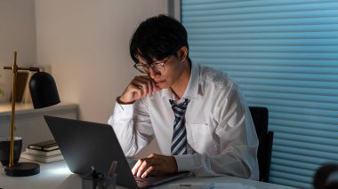 Aşırı çalışma kavramı. Gözlük takan erkek, çenesini sağ eline dayayıp sol elini kullanarak deftere harfler yazıyor..