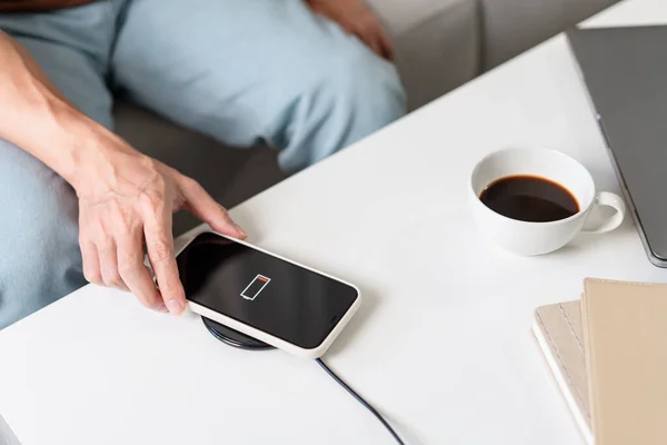 Technology Concept A person with his light blue jeans sitting on the couch and trying to charge his smartphone on the wireless battery charger.