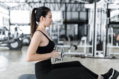 Spor bluzu, dar pantolonu ve siyah spor ayakkabısı giyen kadın oturur ve esnek bir koltuk yuvarlama makinesini çekmeye konsantre olur..