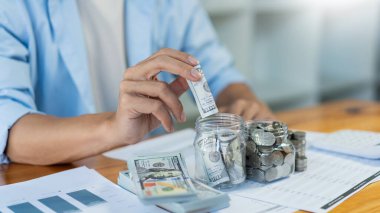 Tasarruf konsepti. Genç bir erkek parayı yuvarlıyor ve şişeye koyuyor..