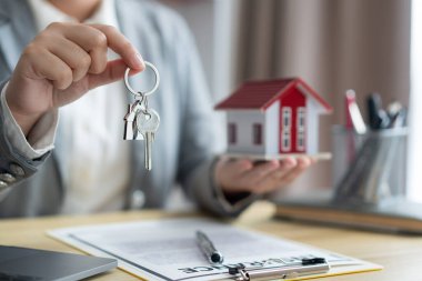 Sigorta konsepti. Emlak temsilcisi sağ elinde evin anahtarı, sol elinde de ev modeli tutuyor..