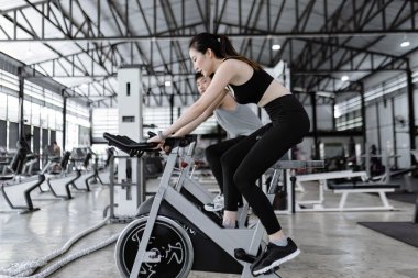 Egzersiz konsepti. İyi görünümlü bayan ve kaslı adam spor bisikletleri sürerken sohbet ederken eğleniyorlar..