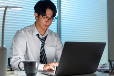 Fazla mesai. Ofis personeli masasında oturmuş, evrak okuyor ve not defterine yazı yazıyor.