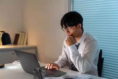 Fazla mesai. Ofis personeli masasında oturmuş, evrak okuyor ve not defterine yazı yazıyor.